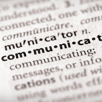 Close-up of a dictionary page highlighting the word “communicator” with its pronunciation and definition in bold text.